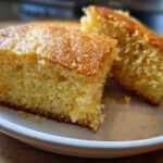 Close-up of two golden slices of moist buttermilk cornbread with a slightly browned top, served on a white plate.
