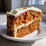 Close-up of a thick slice of moist carrot cake recipe with two layers and generous cream cheese frosting.