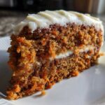 Close-up of a moist slice from a two-layer carrot cake recipe topped with thick cream cheese frosting.