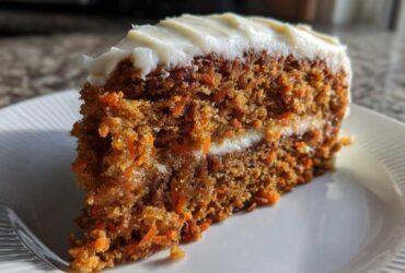 Close-up of a moist slice from a two-layer carrot cake recipe topped with thick cream cheese frosting.