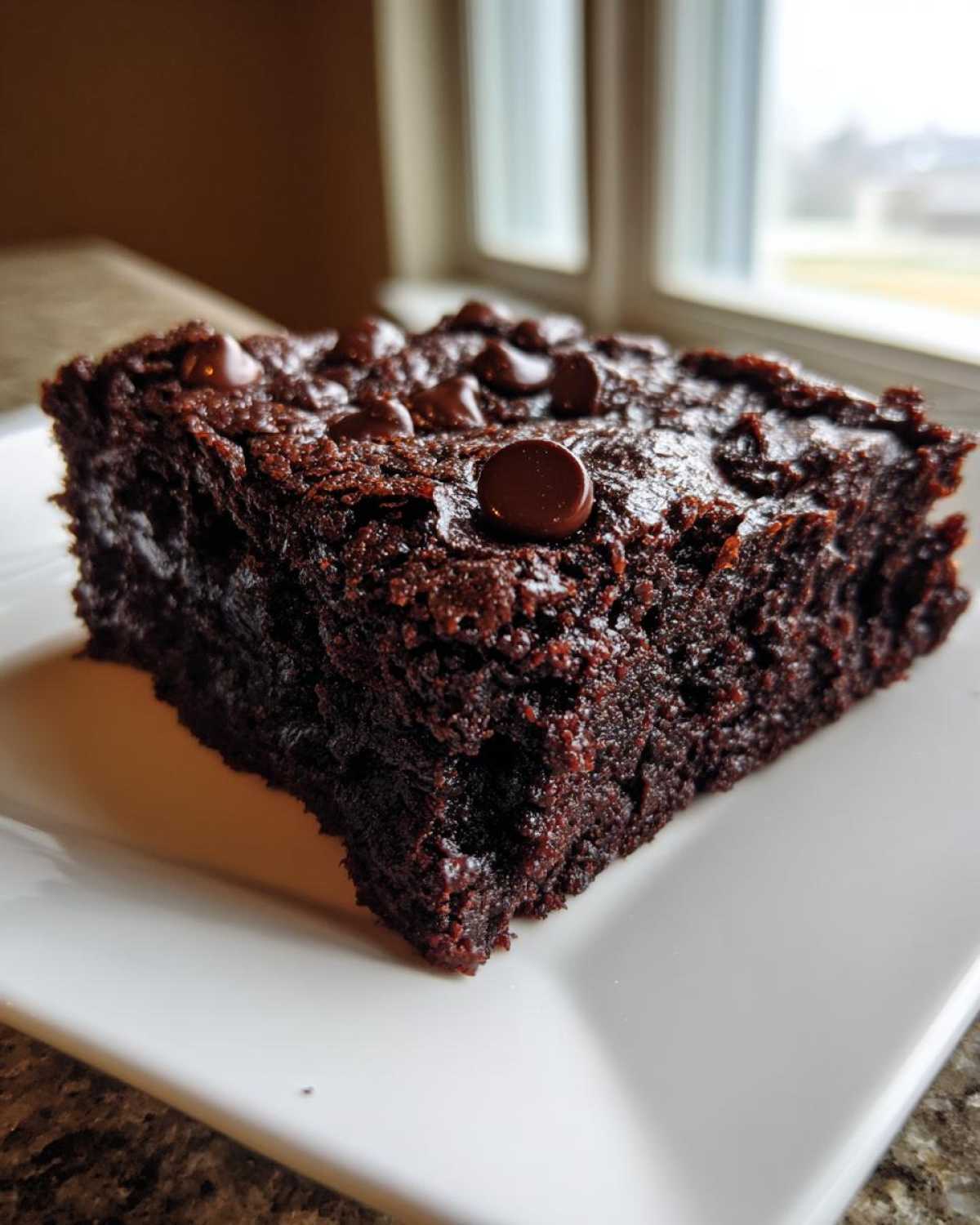 A close-up of a rich, dark slice of black bean brownies topped with melted chocolate chips.