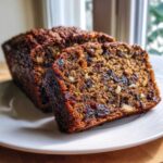 Close-up of a thick slice of moist date nut bread showing visible dates and walnuts, served on a white plate.