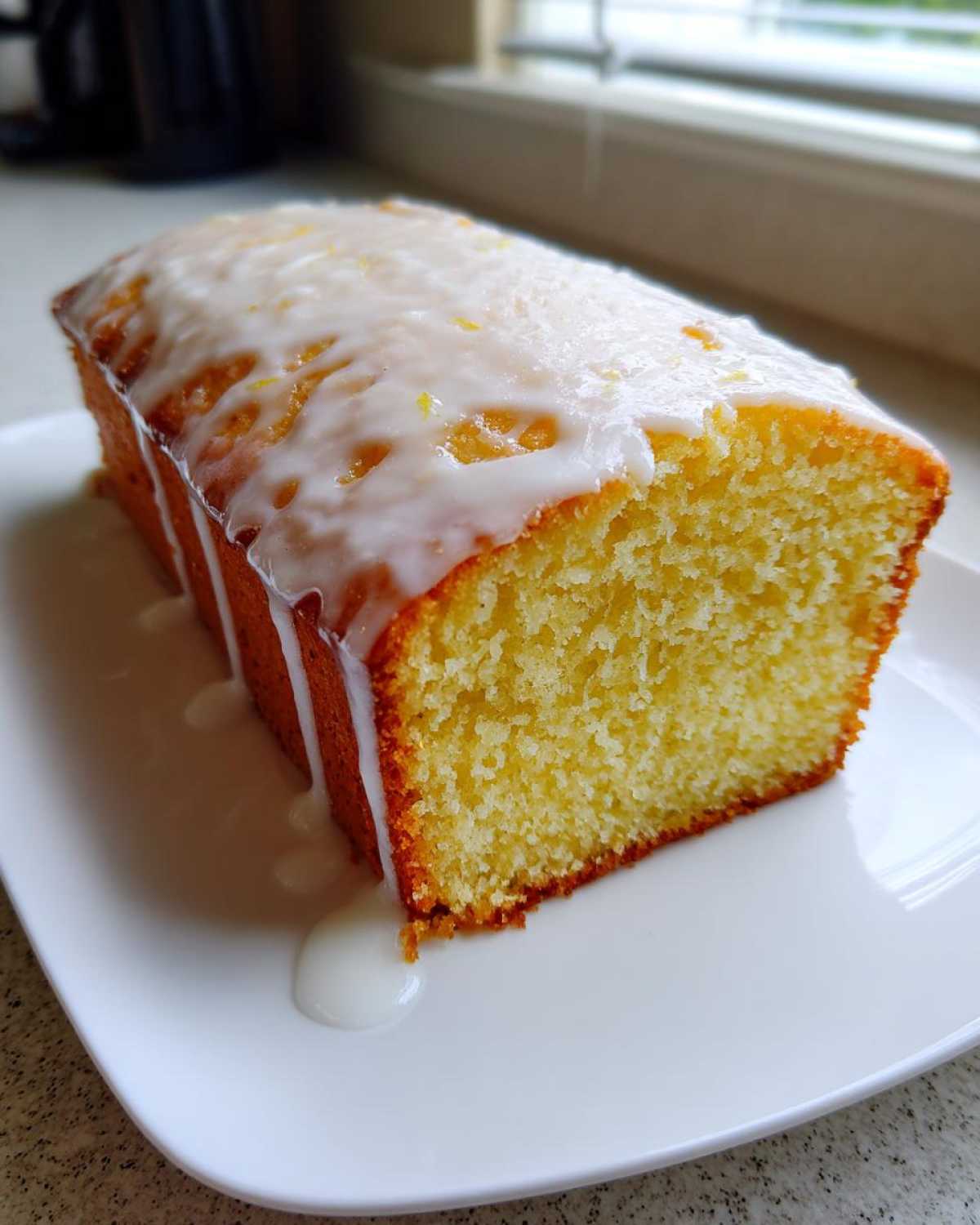 A slice of moist lemon pound cake topped with a thick white lemon glaze dripping down the sides.