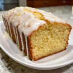 A moist slice of lemon pound cake topped with a thick white glaze and lemon zest.