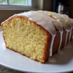 A slice of moist lemon pound cake topped with thick white glaze and lemon zest.