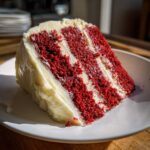 A close-up, tempting slice of moist red velvet cake layered with thick cream cheese frosting.