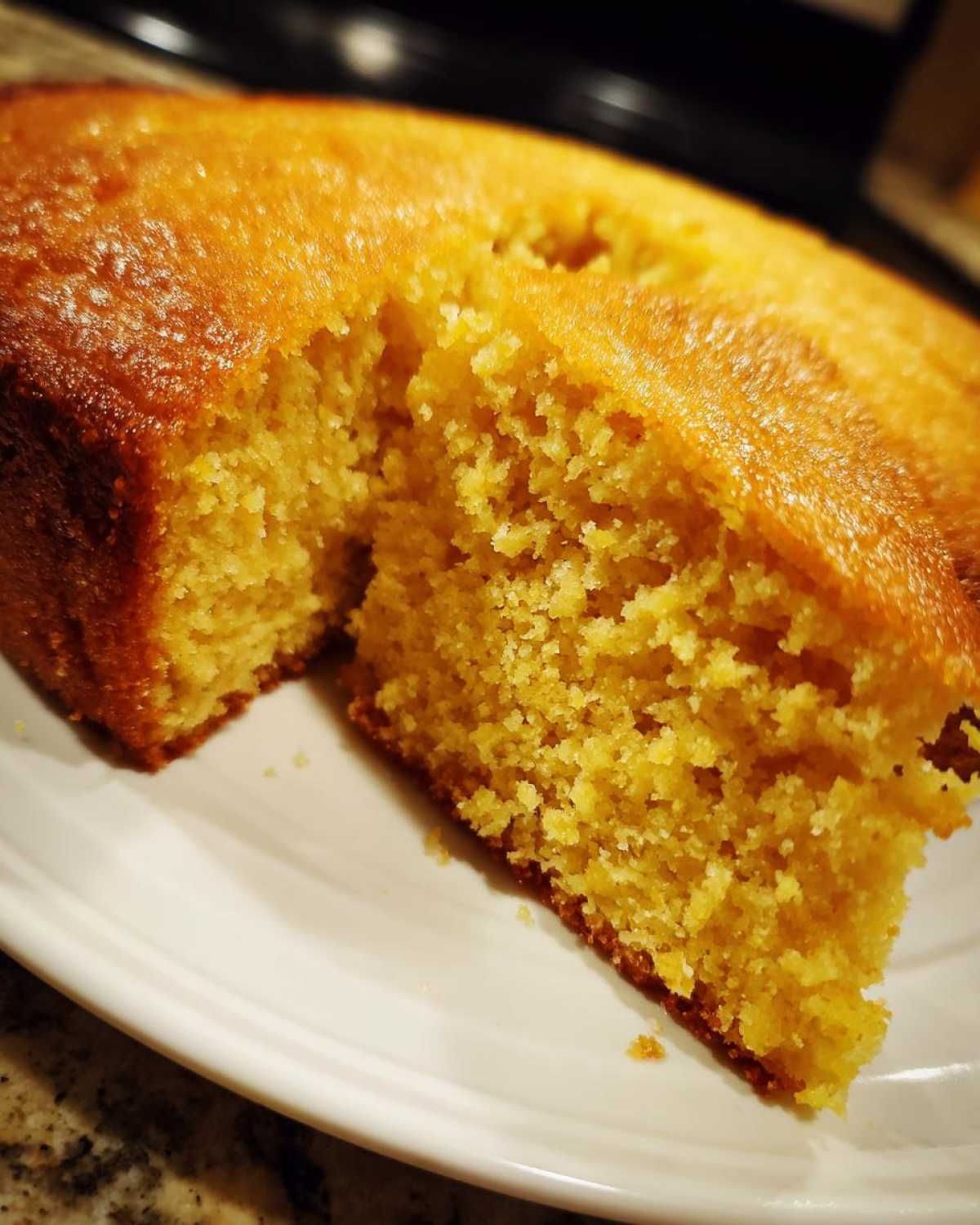 Close-up of a slice of golden, moist skillet cornbread showing its crumb texture on a white plate.