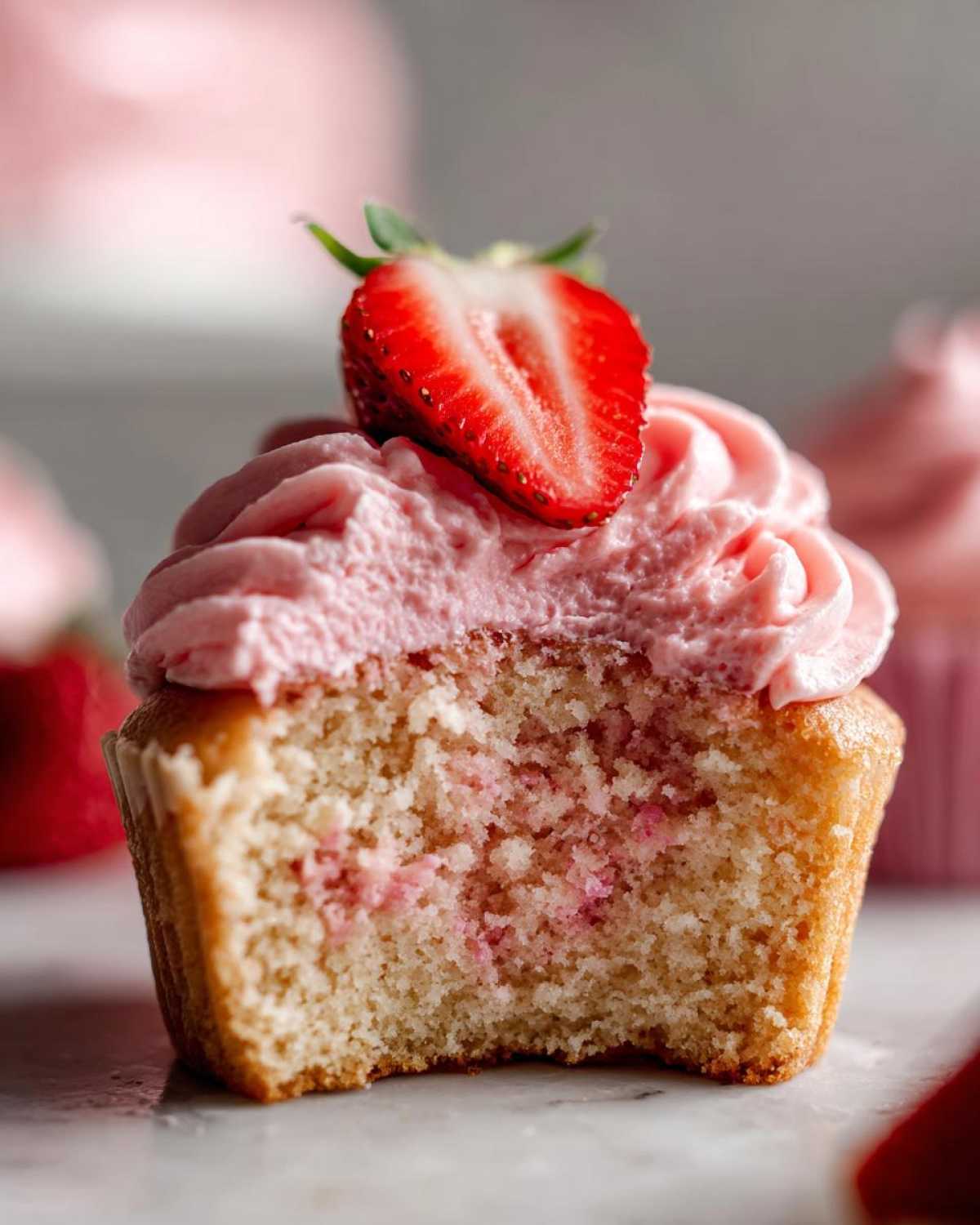 Close-up of a strawberry cupcakes with a bite taken out, showing the moist crumb and pink strawberry frosting.