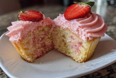 Cross-section view of moist strawberry cupcakes showing pink frosting and fresh strawberry slices on top.