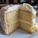 Close-up of a moist slice from a two-layer vanilla cake recipe with creamy white frosting.