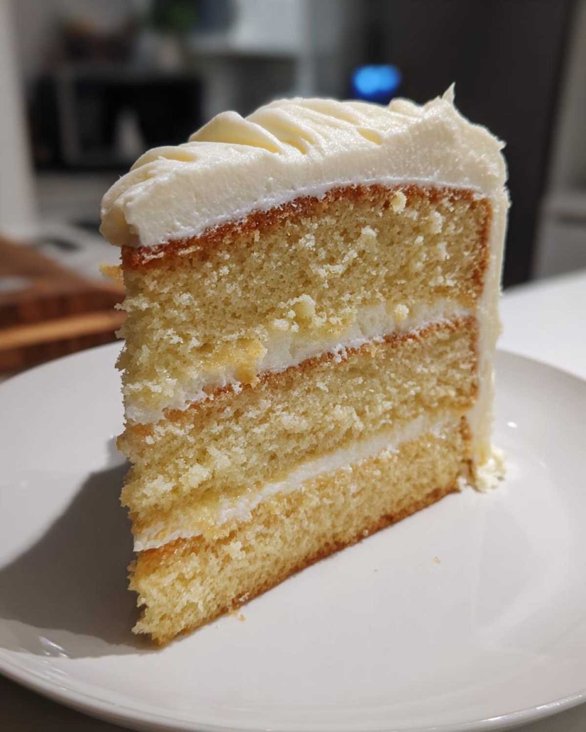 Close-up of a moist slice of three-layer vanilla cake recipe with white frosting.