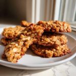 Close-up of a stack of golden brown, chewy breakfast cookie made with visible oats, one cookie broken open.