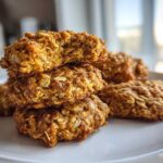 A stack of four golden brown, textured breakfast cookie treats made with visible oats, one on top is broken open.