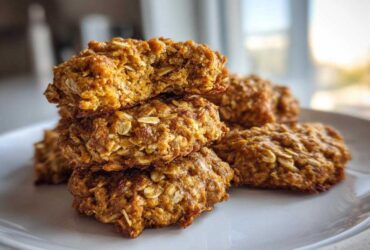 A stack of four golden brown, textured breakfast cookie treats made with visible oats, one on top is broken open.
