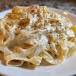 Close-up of fettuccine pasta generously coated in creamy Olive Garden Alfredo Sauce and topped with black pepper.