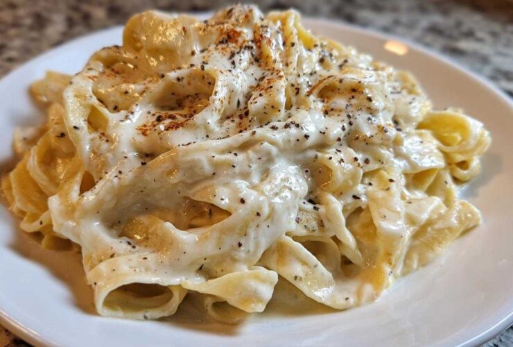 Close-up of fettuccine pasta generously coated in creamy Olive Garden Alfredo Sauce and topped with black pepper.