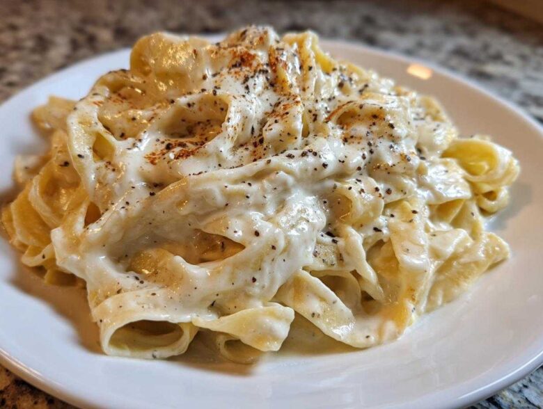 Close-up of fettuccine pasta generously coated in creamy Olive Garden Alfredo Sauce and topped with black pepper.