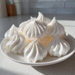 A pile of perfectly piped, bright white meringue cookies resting on a small white plate.