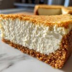 Close-up of a thick slice of creamy Protein Cheesecake showing the dense filling and golden graham cracker crust.