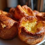Close-up of several golden brown, perfectly risen yorkshire pudding pastries piled on a white plate.