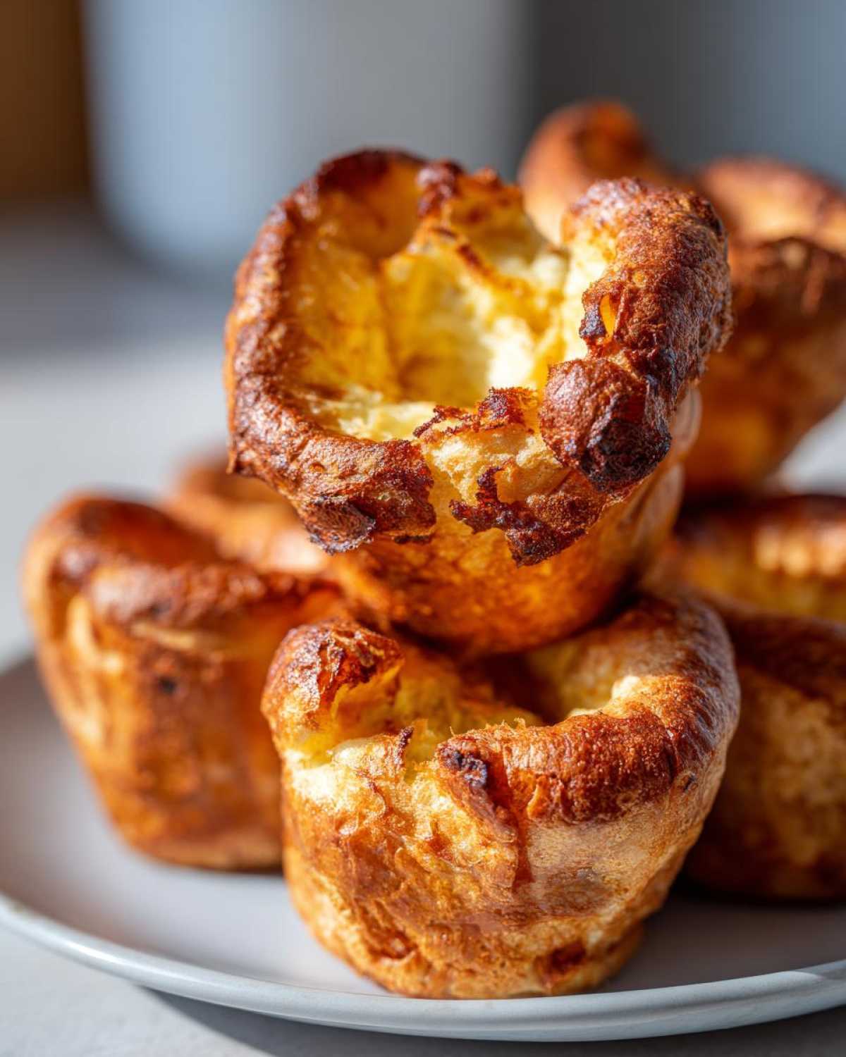 Close-up of several golden brown, perfectly risen Yorkshire pudding piled on a light gray plate.