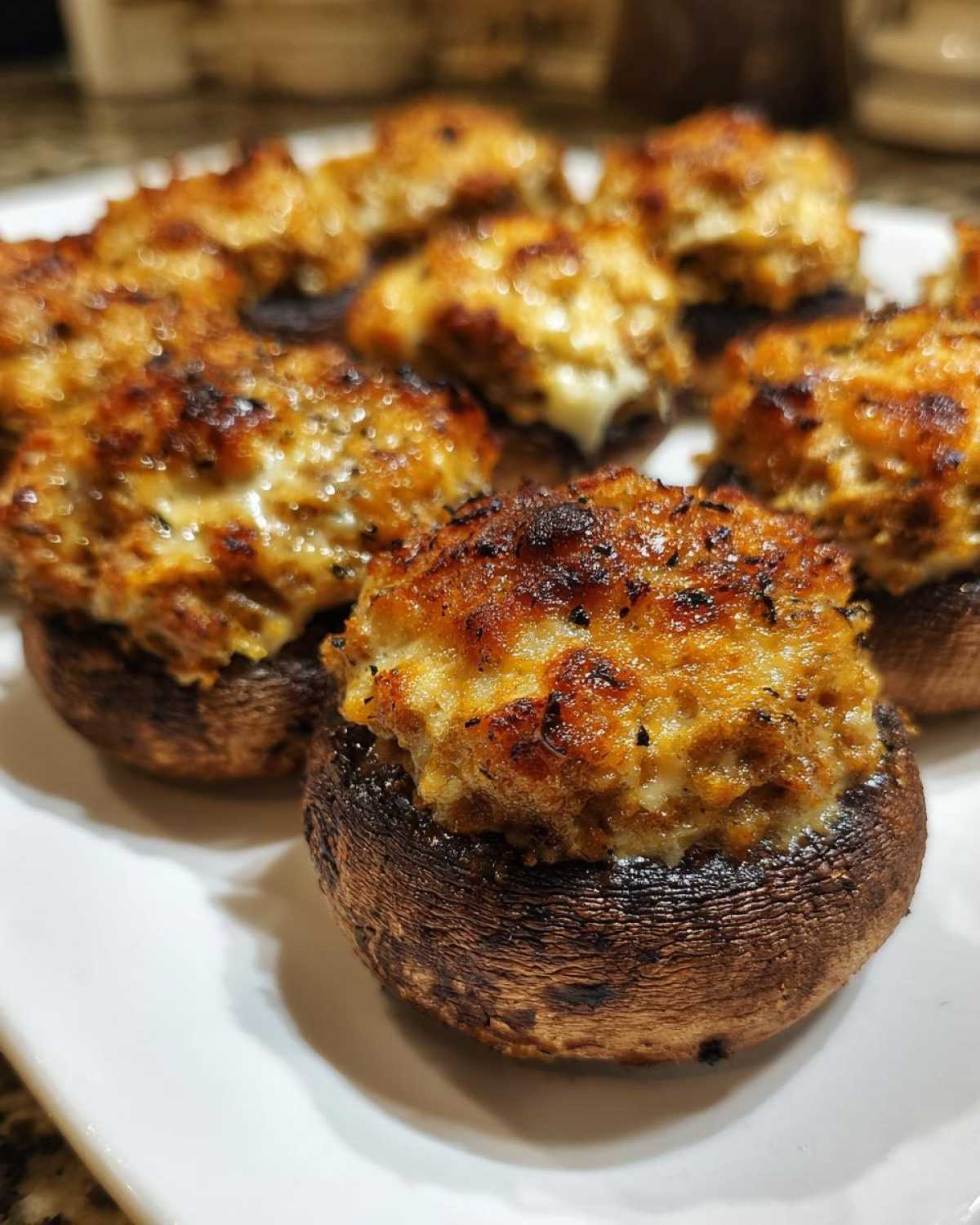 Close-up of golden-brown, baked Sausage stuffed mushrooms piled high with savory filling on a white serving platter.