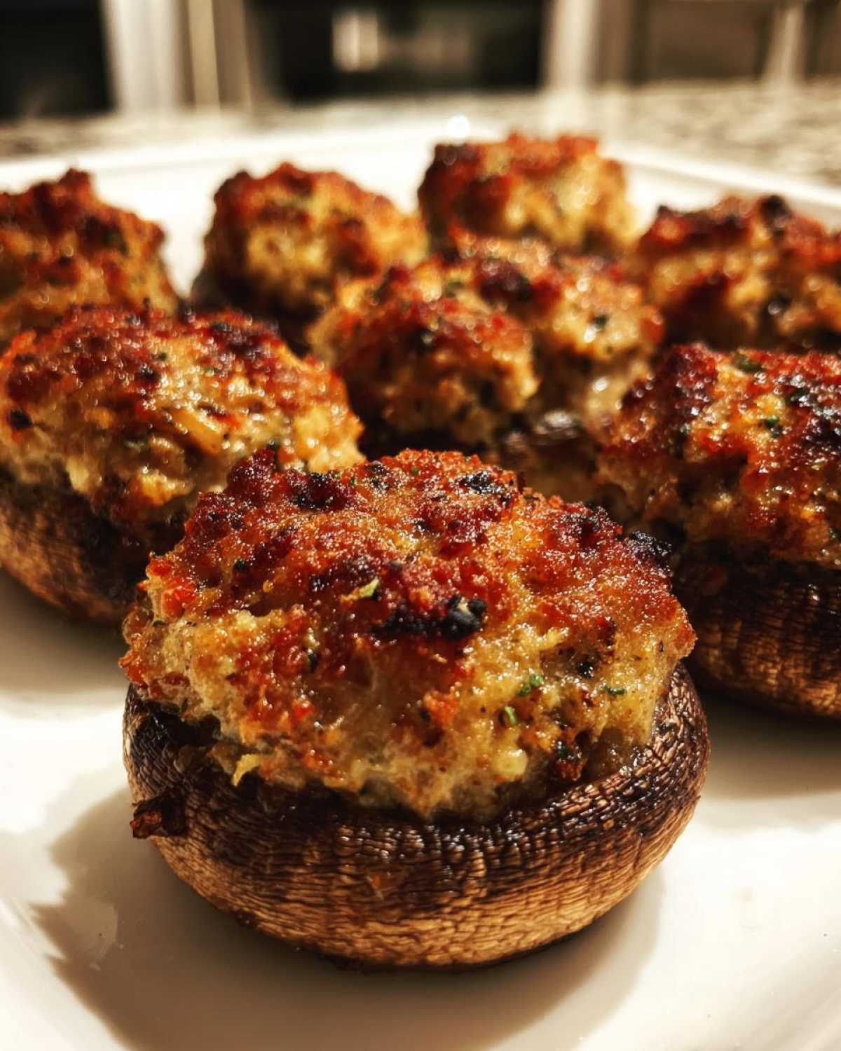 Close-up of several golden-brown, baked Sausage stuffed mushrooms arranged on a white plate.