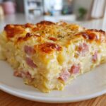 A thick, square slice of creamy scalloped potatoes and ham casserole with a golden, bubbly cheese crust.