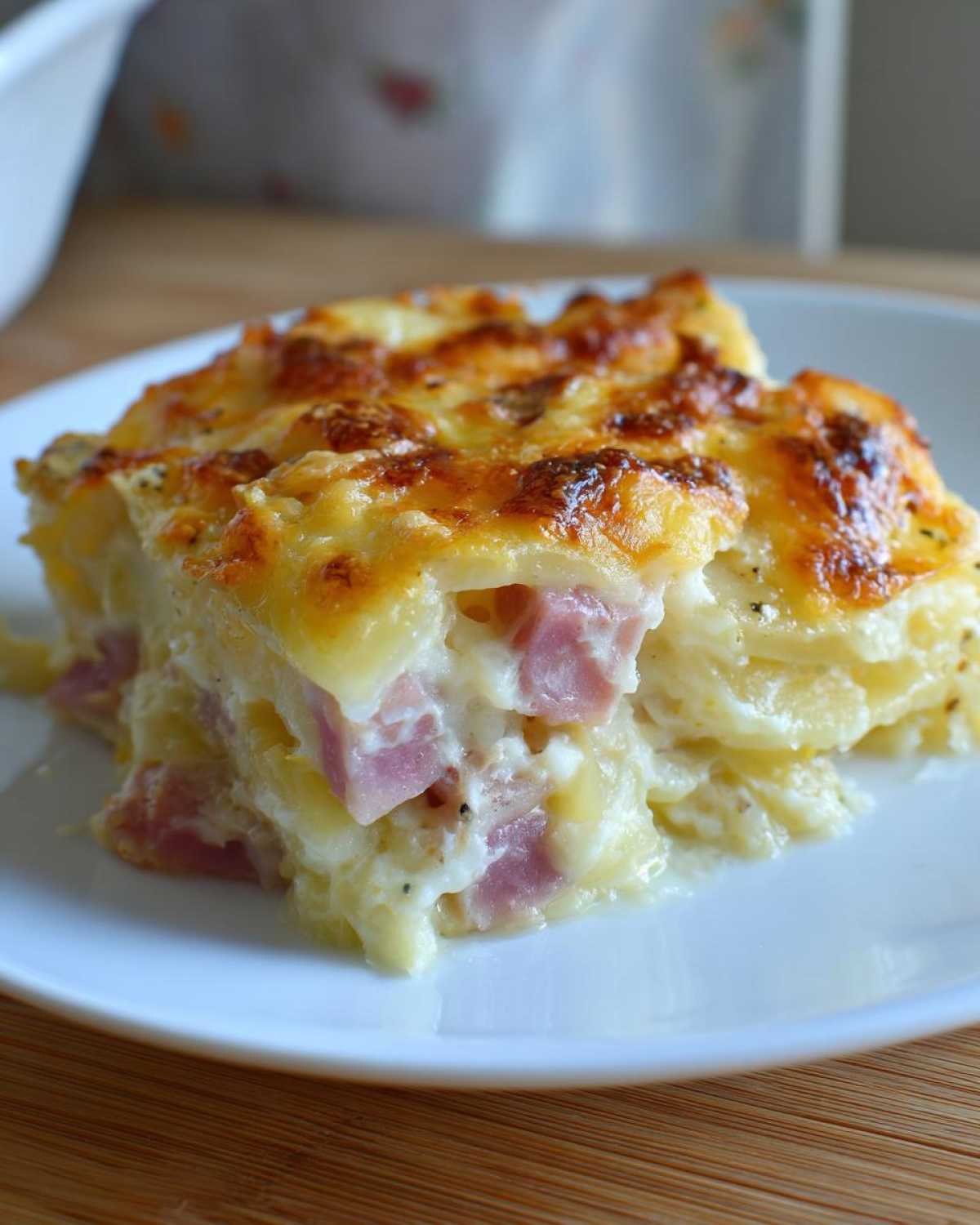 A close-up slice of creamy scalloped potatoes and ham casserole topped with melted, browned cheese.