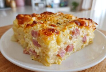 A thick, square slice of creamy scalloped potatoes and ham casserole with a golden, bubbly cheese crust.