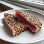 Two thick slices of perfectly Seared Ahi Tuna showing a deep red center and a heavy sesame seed crust.