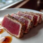 Four slices of perfectly seared tuna steak with a black pepper crust, served with a light sauce, showcasing the MARINADE FOR TUNA STEAK results.