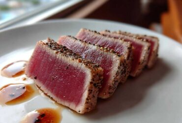 Four slices of perfectly seared tuna steak with a black pepper crust, served with a light sauce, showcasing the MARINADE FOR TUNA STEAK results.