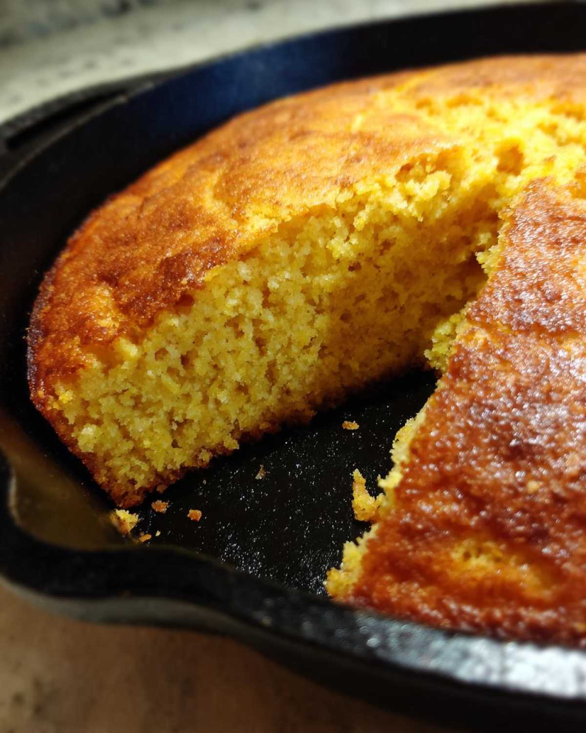 Close-up of golden brown skillet cornbread with a piece cut out, showing the moist interior texture.