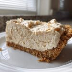 A generous slice of creamy peanut butter pie with a thick graham cracker crust, served on a white plate.