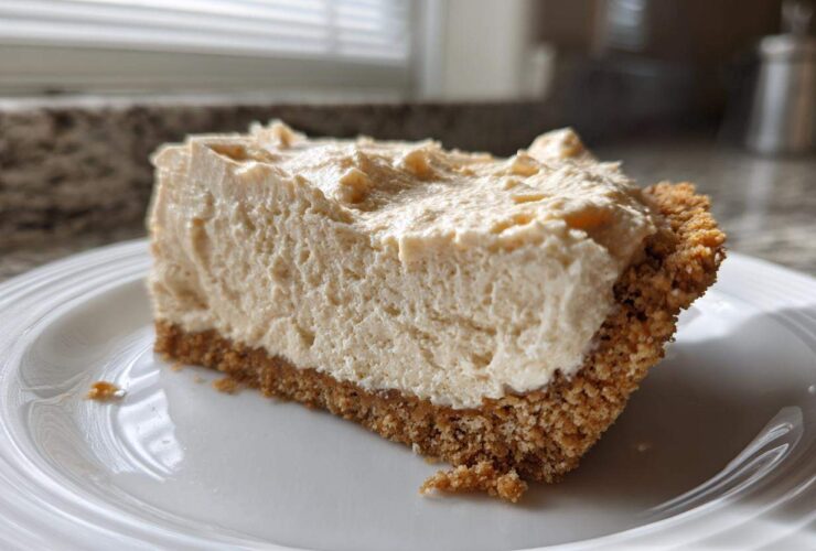 A generous slice of creamy peanut butter pie with a thick graham cracker crust, served on a white plate.