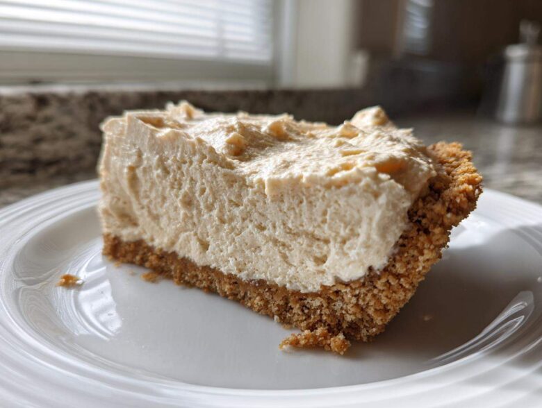 A generous slice of creamy peanut butter pie with a thick graham cracker crust, served on a white plate.