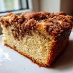 A close-up slice of moist sour cream coffee cake featuring a marbled cinnamon swirl and thick, crumbly streusel topping.