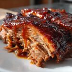 Close-up of tender, shredded Slow Cooker Pulled Pork coated in a thick, glossy BBQ sauce on a white plate.