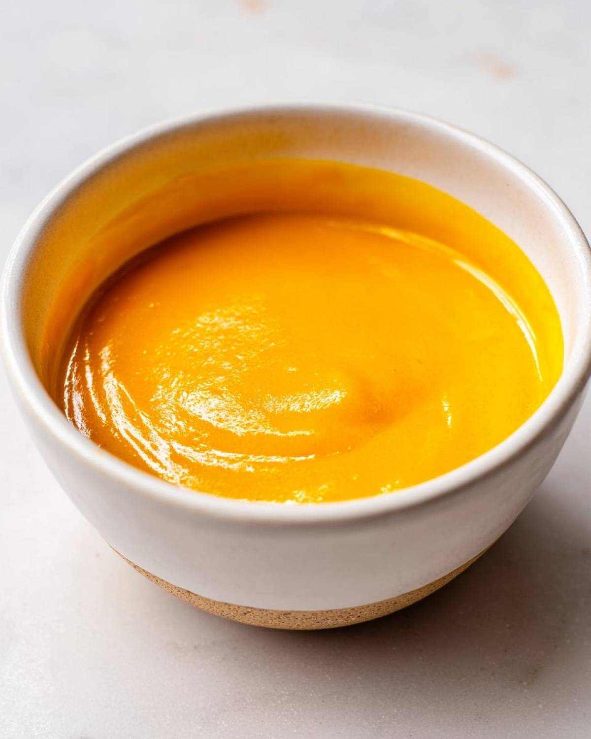 Close-up of vibrant, smooth nacho cheese sauce filling a small white ceramic bowl.