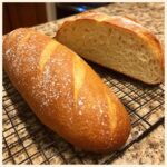 A golden-brown, freshly baked French bread loaf, one half sliced to show the soft interior crumb.