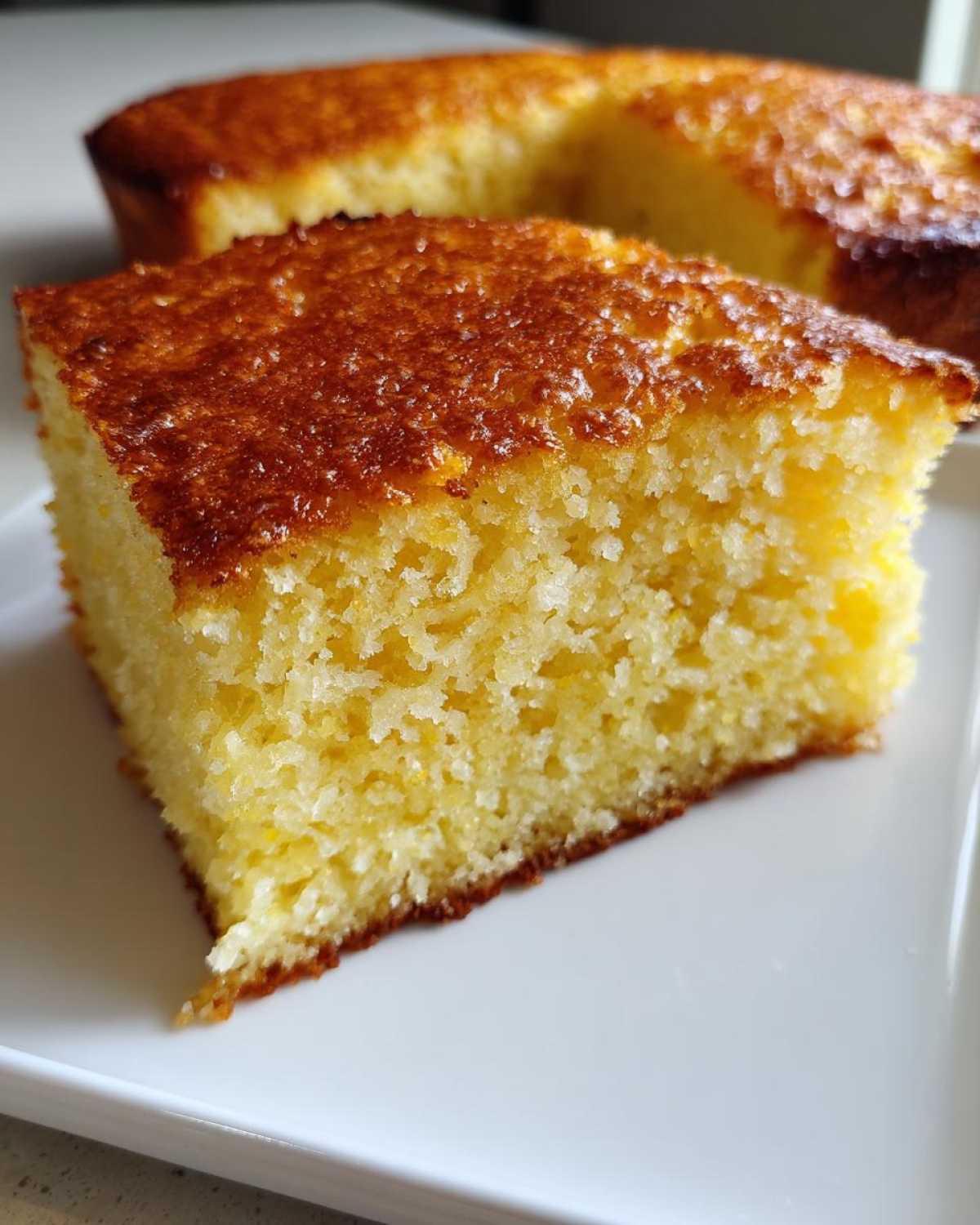 A close-up of a moist slice of golden yellow sourdough cornbread resting on a white plate.