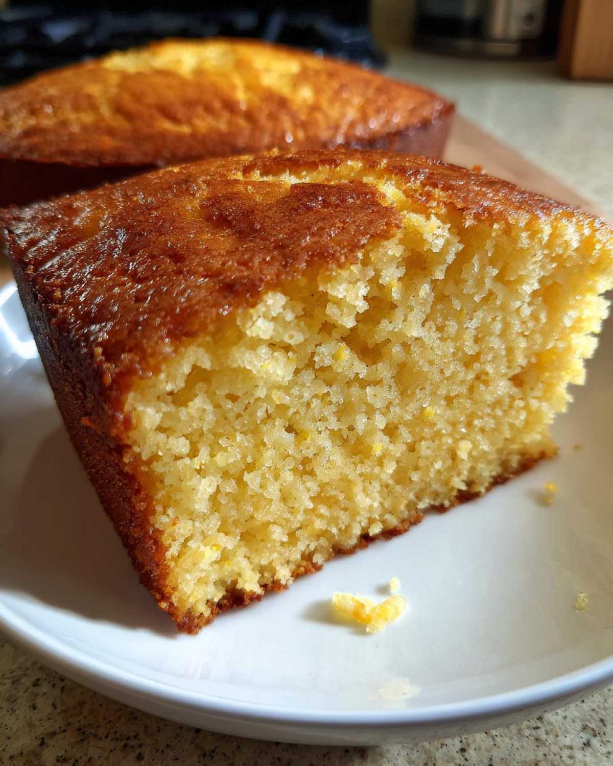 Close-up of a moist, golden slice of sourdough cornbread on a white plate.