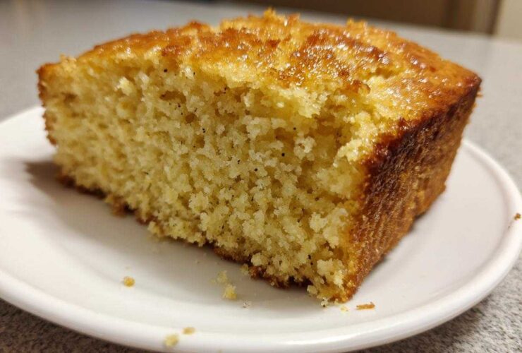 Close-up of a thick slice of golden sourdough cornbread with a shiny, sweet glaze on top, sitting on a white plate.