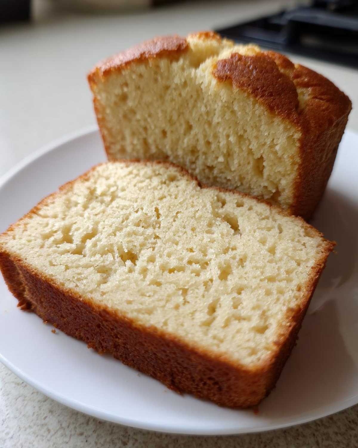 Close-up of two slices of golden-brown sourdough cornbread resting on a white plate.