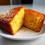 Two golden-brown squares of moist sourdough cornbread cut open on a white plate.