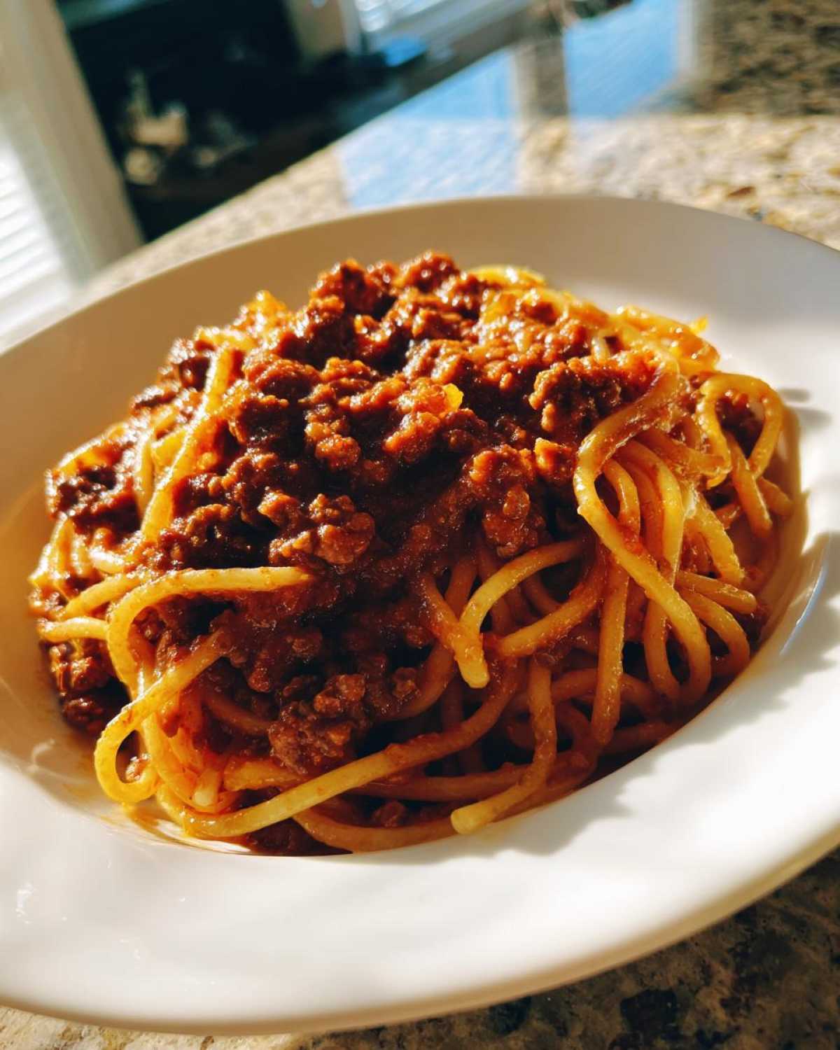 A close-up of spaghetti generously topped with rich, meaty bolognese sauce in a white bowl.
