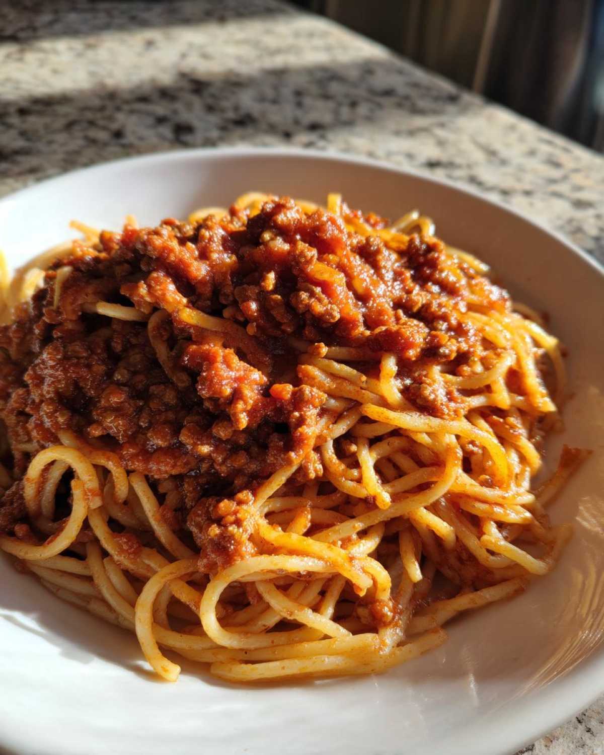 A close-up of spaghetti generously topped with rich, meaty bolognese sauce in a white bowl.