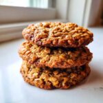 A vertical stack of three golden brown, textured oatmeal cookie treats on a white surface.