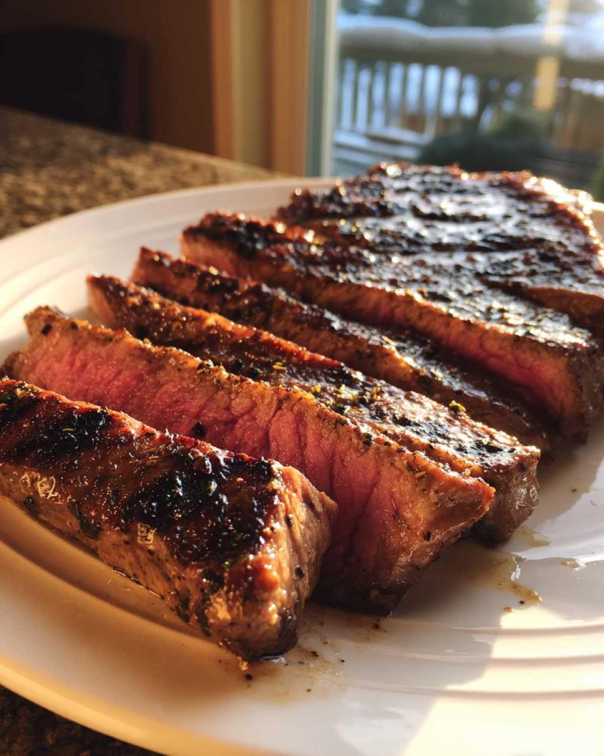 Slices of medium-rare steak, glistening with marinade, served on a white plate.